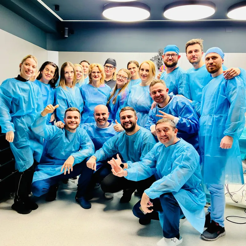Grup de medici în halate albastre la finalul unui curs, zâmbind spre cameră.